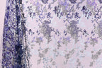 a fabric with a floral pattern in shades of purple and gray, with some white accents. The fabric appears to be a sheer or sheer-like material, with a delicate and intricate design.