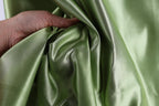 A hand is holding a piece of green satin fabric, which appears to be shiny and smooth.