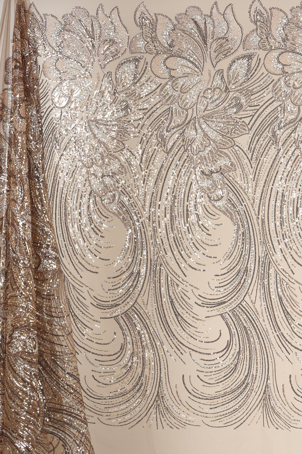 a close-up view of a fabric with a repeating pattern of intricate designs, including floral and wave-like motifs. The fabric appears to be made of shimmering material, adding a touch of sparkle and elegance to the design.