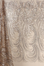 a close-up view of a fabric with a repeating pattern of intricate designs, including floral and wave-like motifs. The fabric appears to be made of shimmering material, adding a touch of sparkle and elegance to the design.
