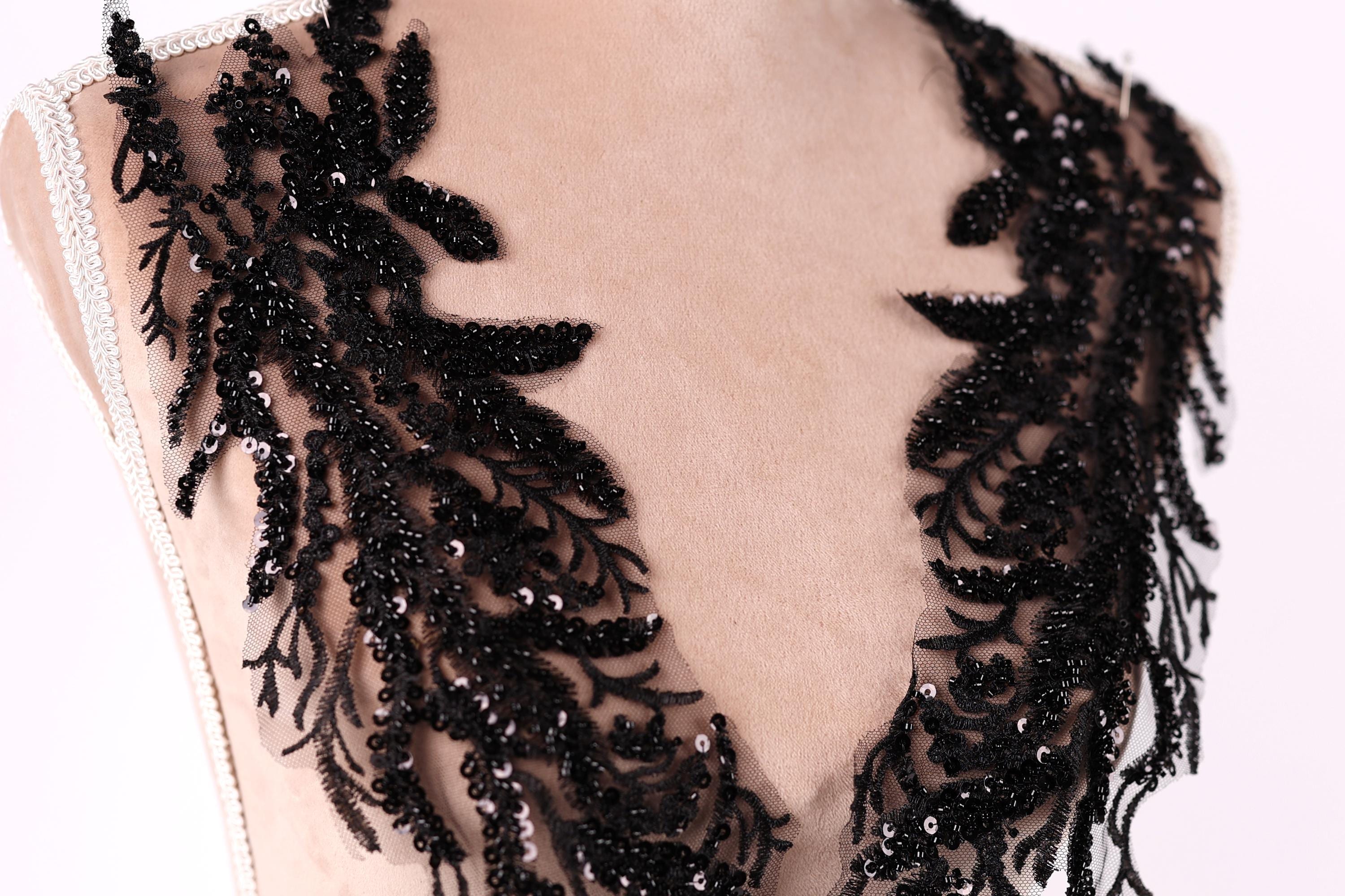 A close-up view of a mannequin torso wearing a black lace dress with intricate black sequin details.