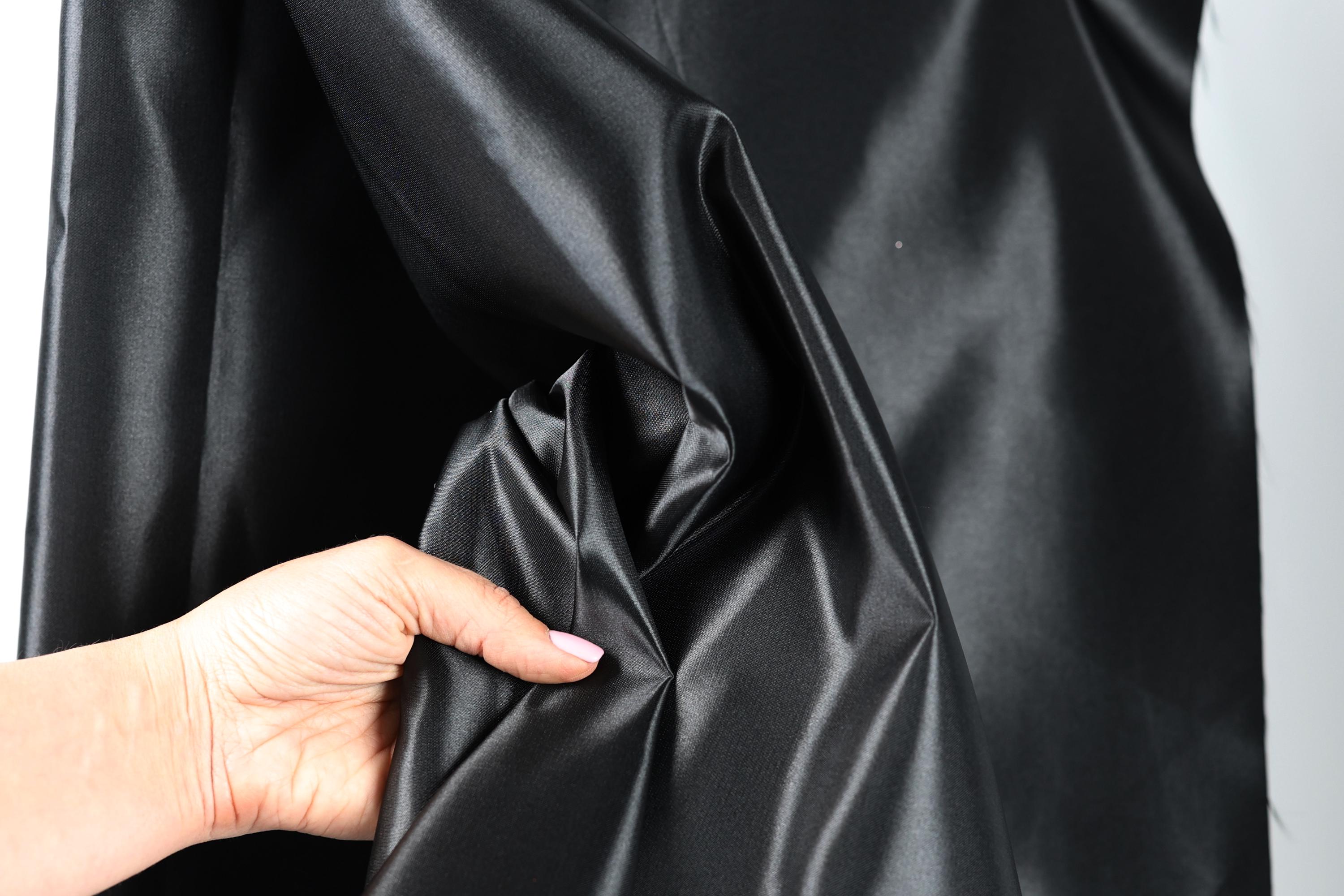 A hand is holding a piece of black satin fabric, which appears to be shiny and smooth.