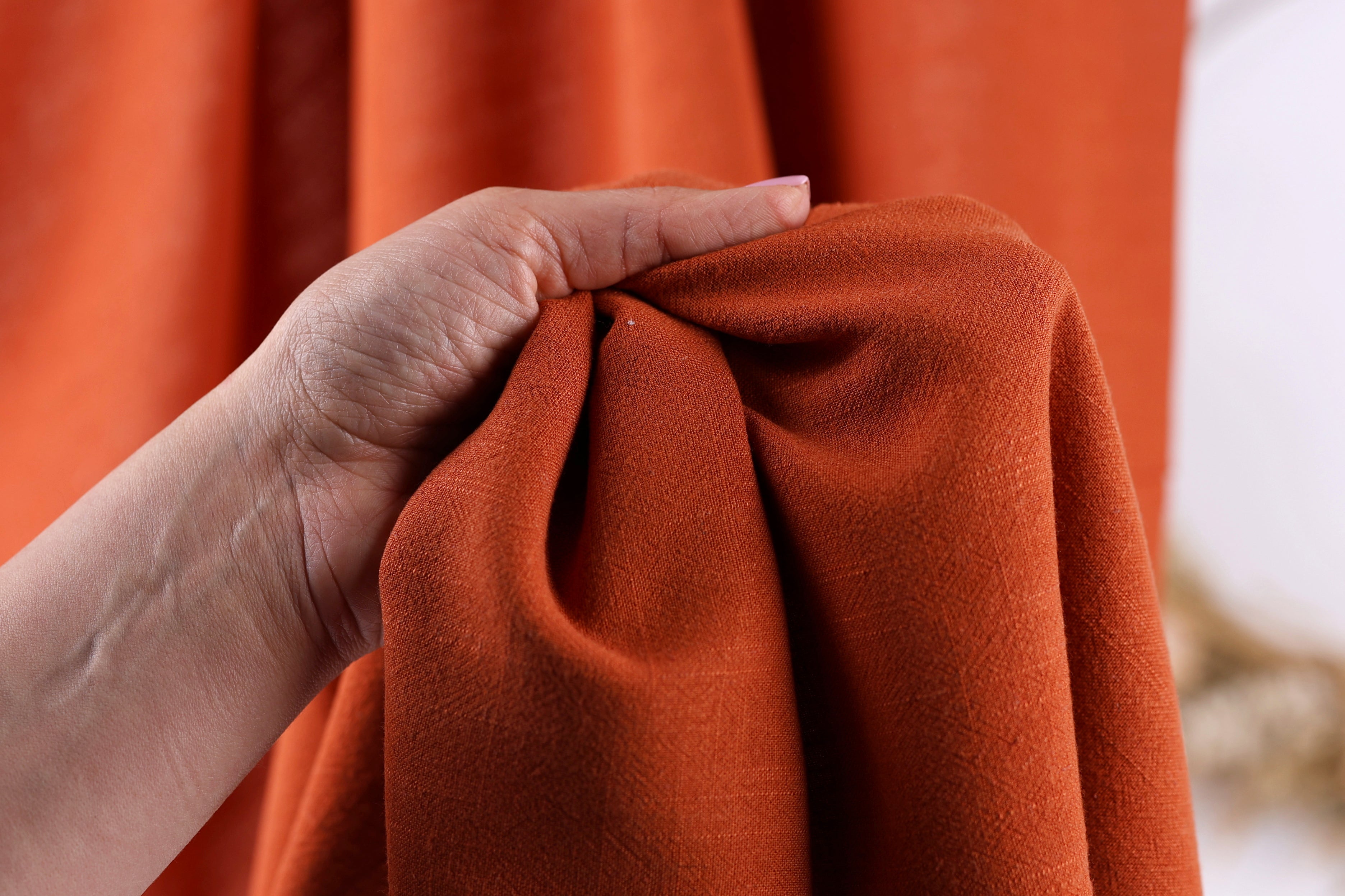 A hand is holding a piece of orange fabric, possibly a curtain or garment, in front of a blurred background.