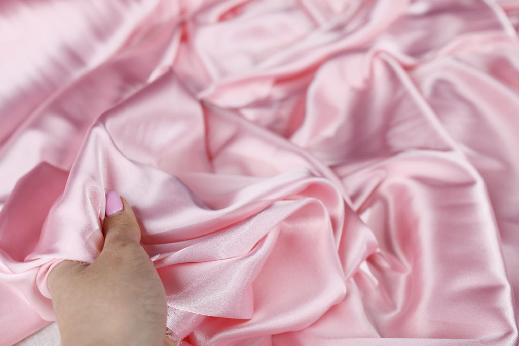 a person&#39;s hand on a pink satin fabric