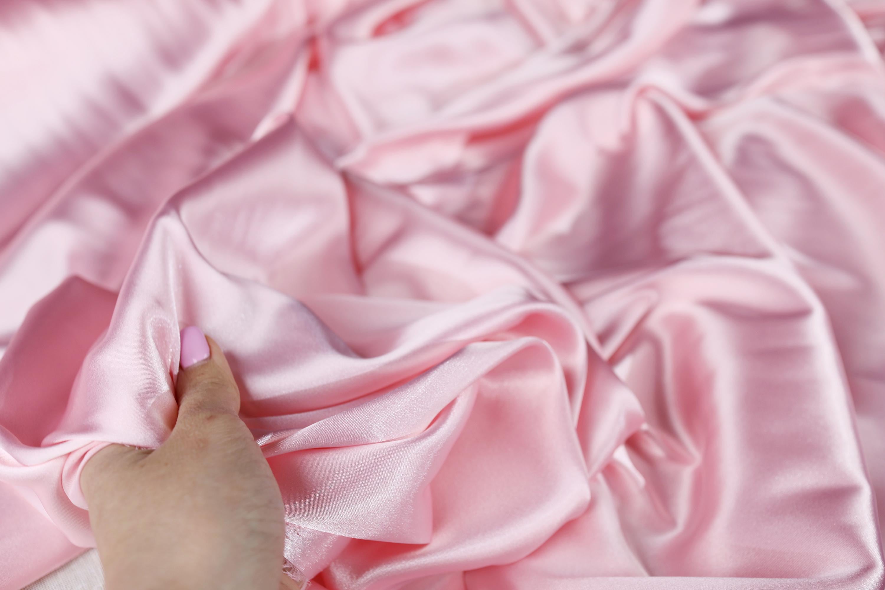 a person&#39;s hand on a pink satin fabric