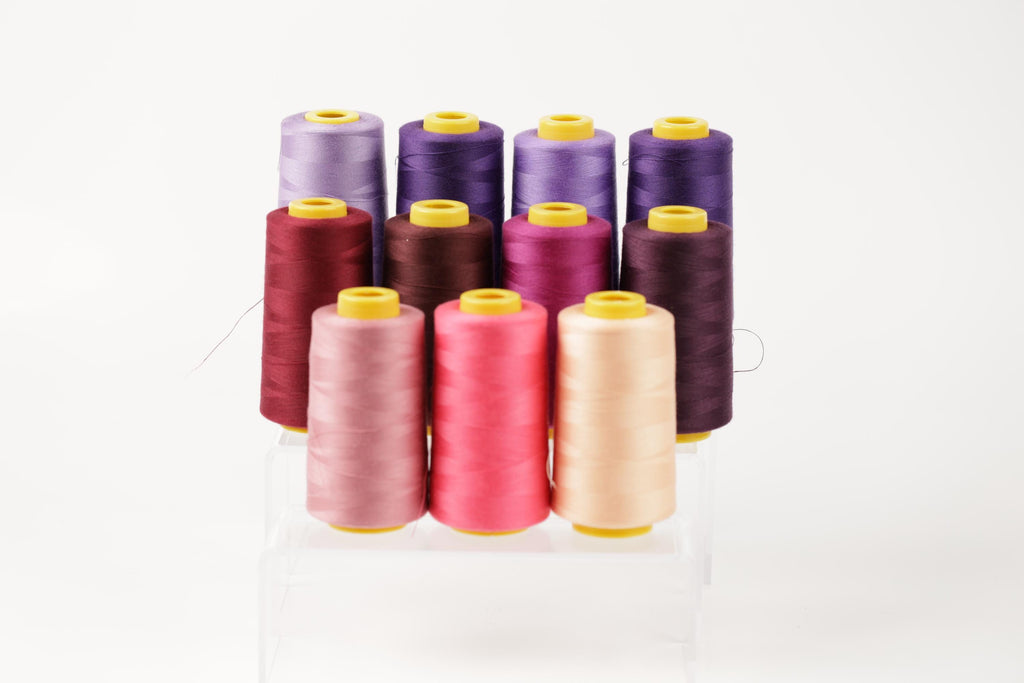 A collection of colorful spools of thread, including pink, purple, and yellow, arranged in a neat row on a white background.