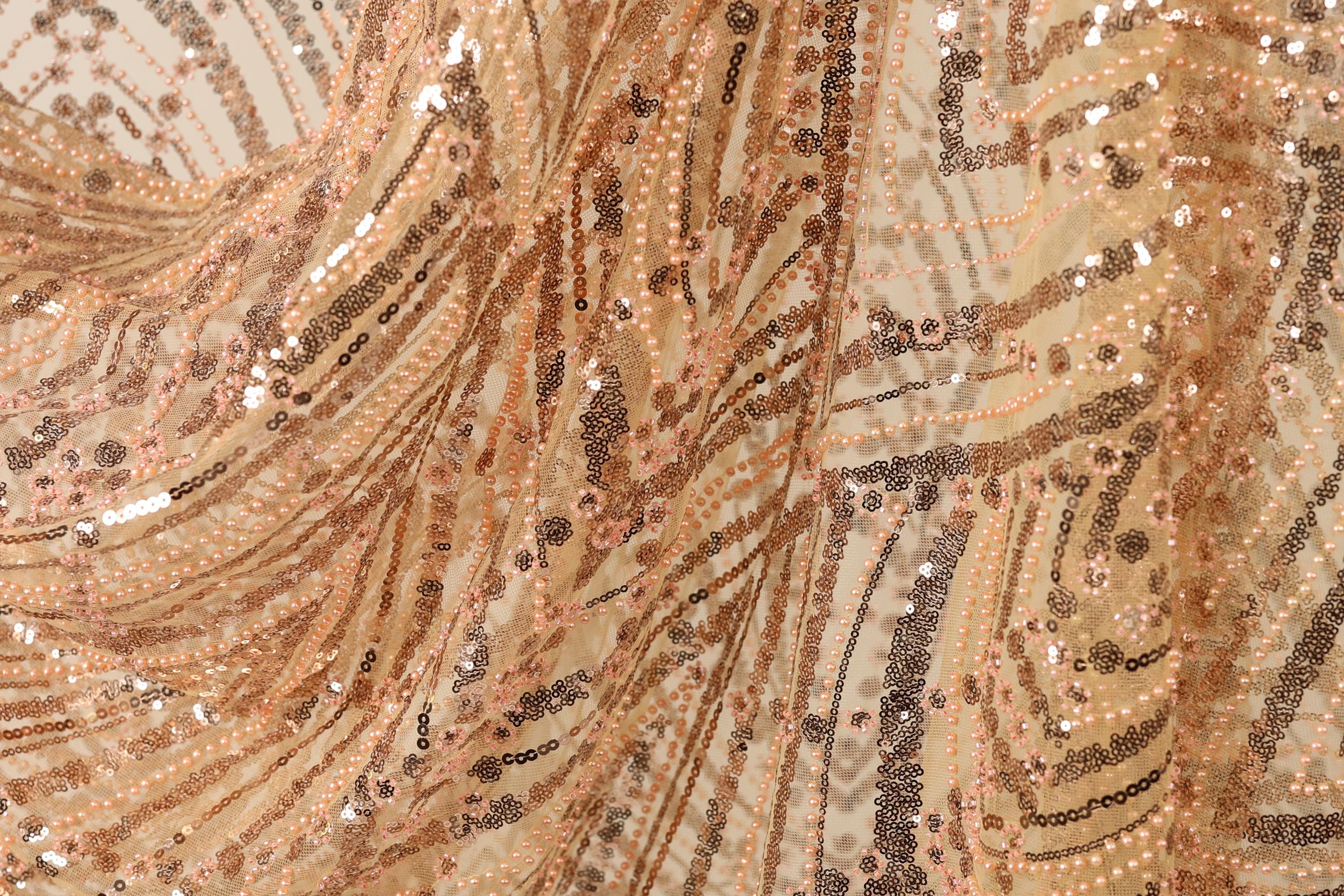 The image is a close-up of a fabric with a gold and black sequin pattern, featuring a swirling and textured appearance.
