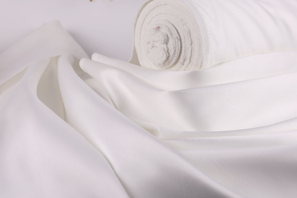 A close-up view of a white fabric, possibly silk or satin, with a rolled-up end visible.