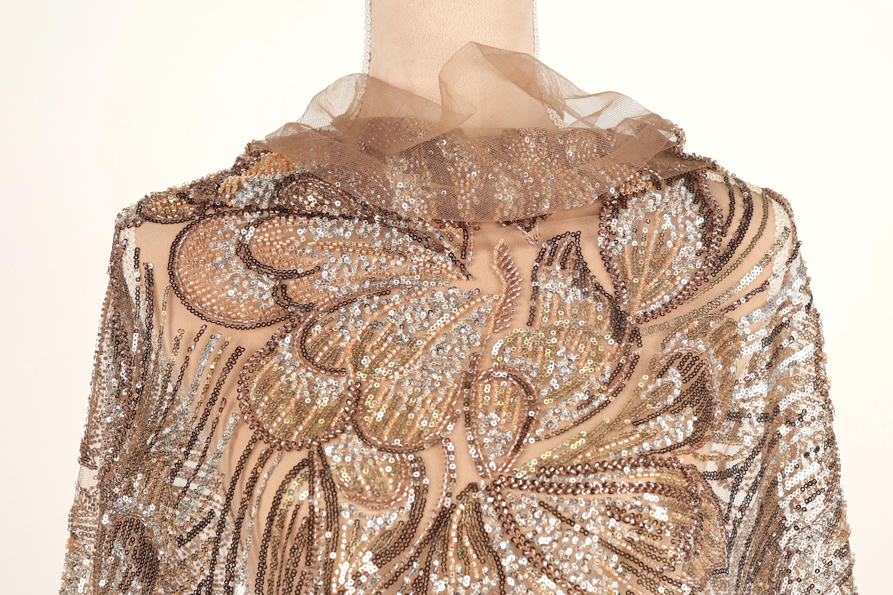 a close-up view of a beige and gold sequined dress with a ruffled collar and a floral pattern.