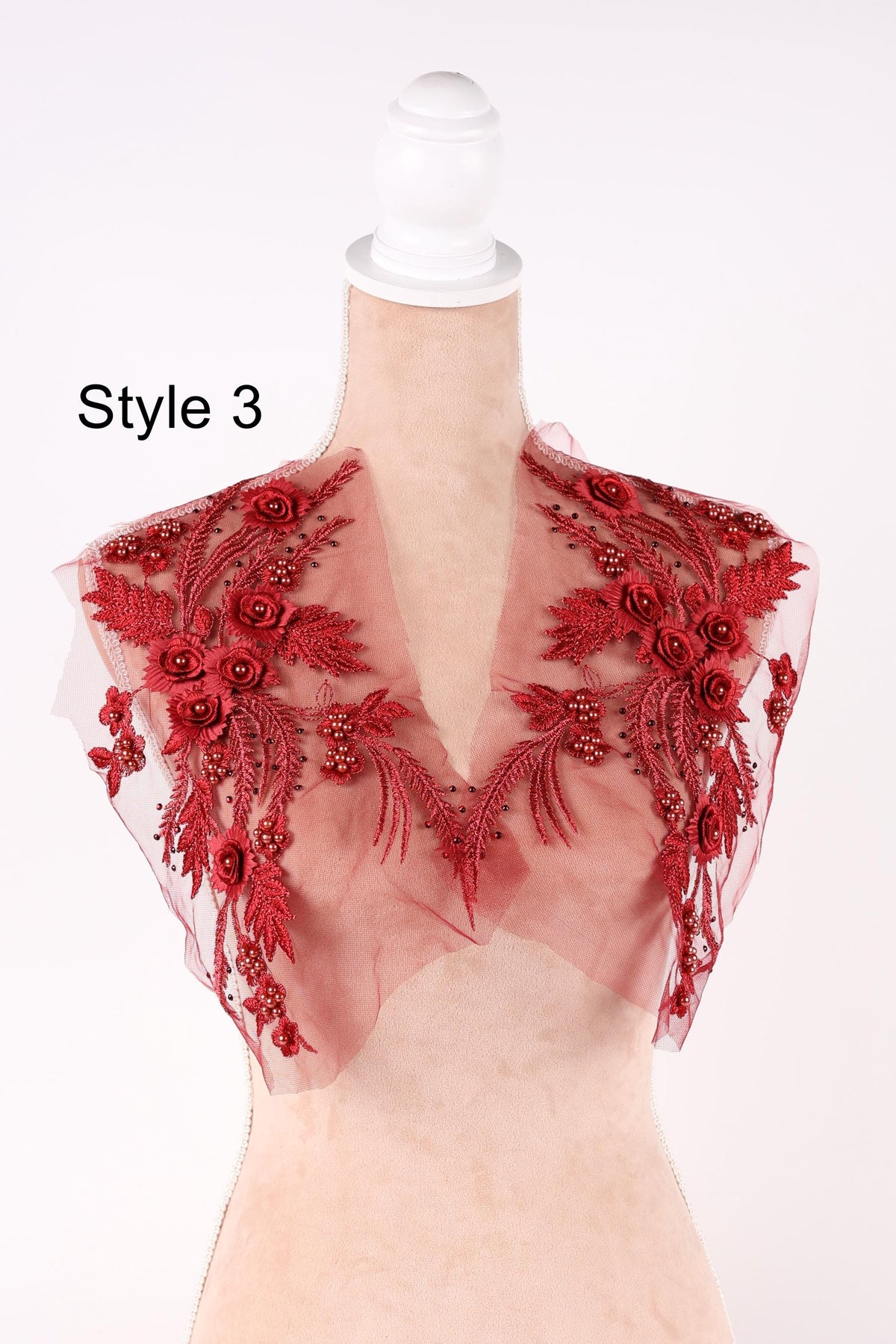 A mannequin wearing a red dress with intricate floral embroidery on the shoulders and neck.