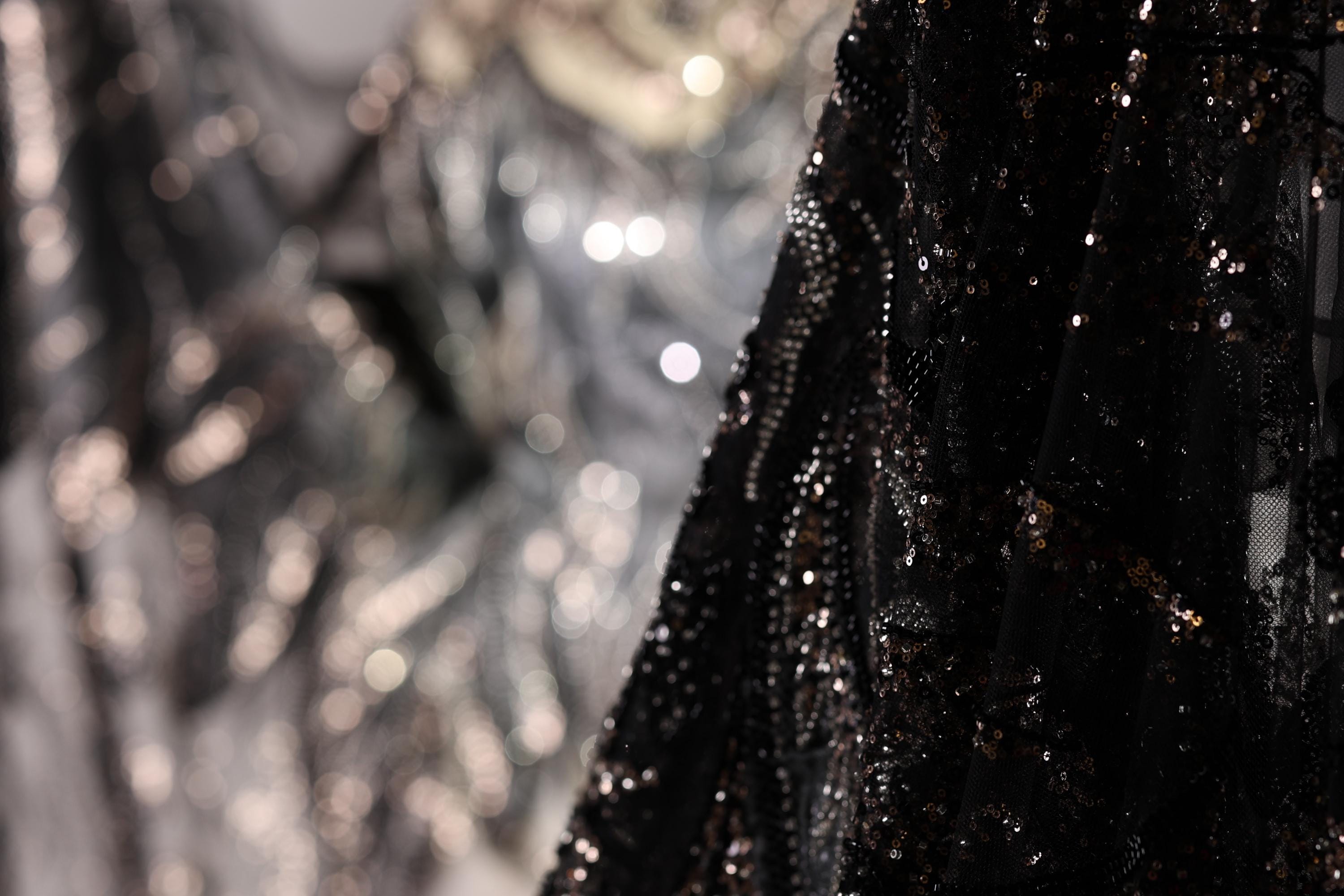 a close-up view of a black sequined fabric, with a blurred background that appears to be a collage of other fabric pieces.