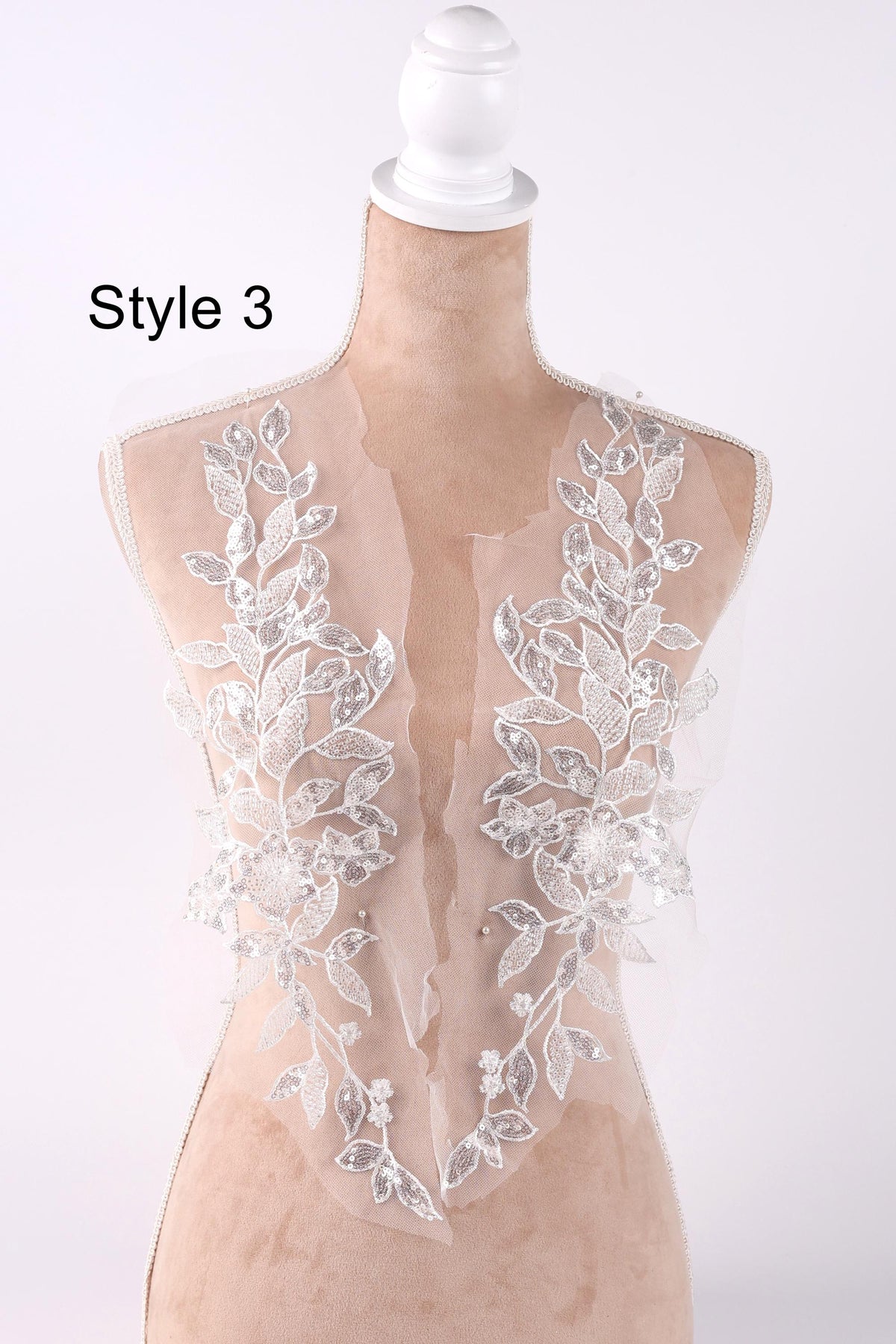 A mannequin wearing a white lace dress with floral embroidery on the front.