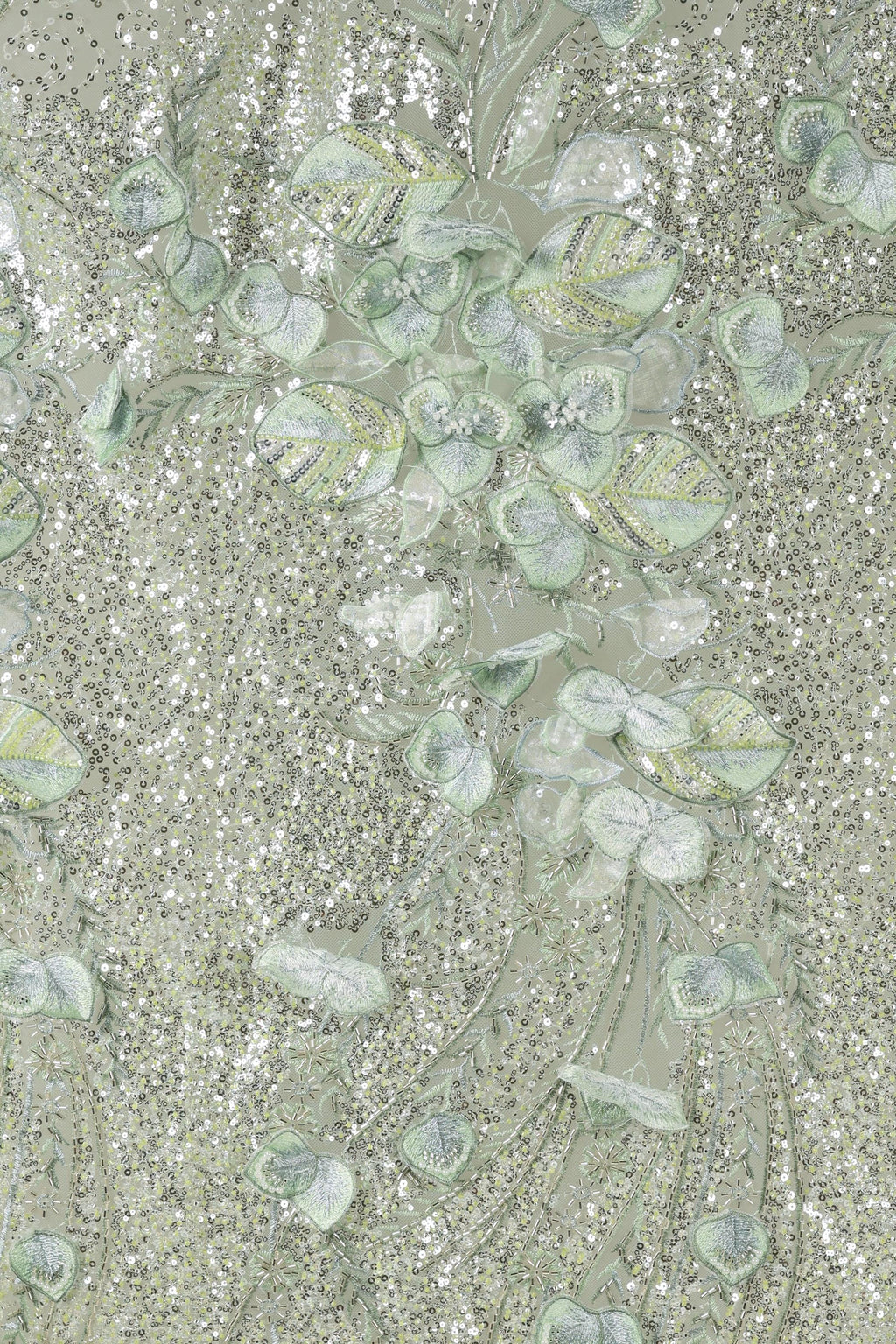 The image is a close-up of a fabric with a floral pattern, featuring a variety of green and white leaves and flowers. The fabric appears to be made of a shiny, glittery material, giving it a sparkling and elegant appearance.