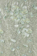 The image is a close-up of a fabric with a floral pattern, featuring a variety of green and white leaves and flowers. The fabric appears to be made of a shiny, glittery material, giving it a sparkling and elegant appearance.