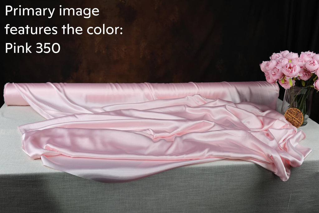 a roll of pink satin fabric, with a vase of pink flowers placed next to it on a table.