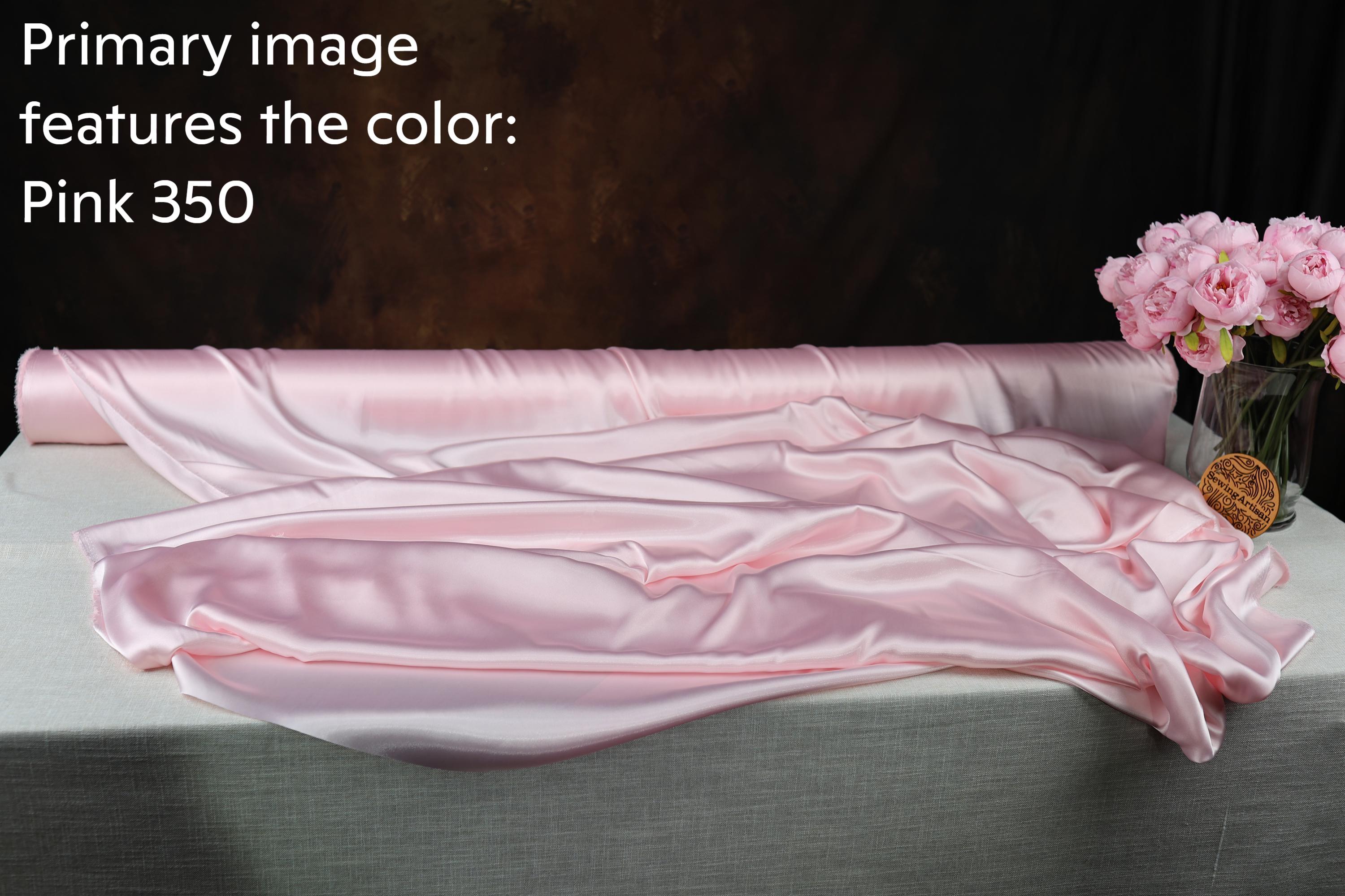 a roll of pink satin fabric, with a vase of pink flowers placed next to it on a table.