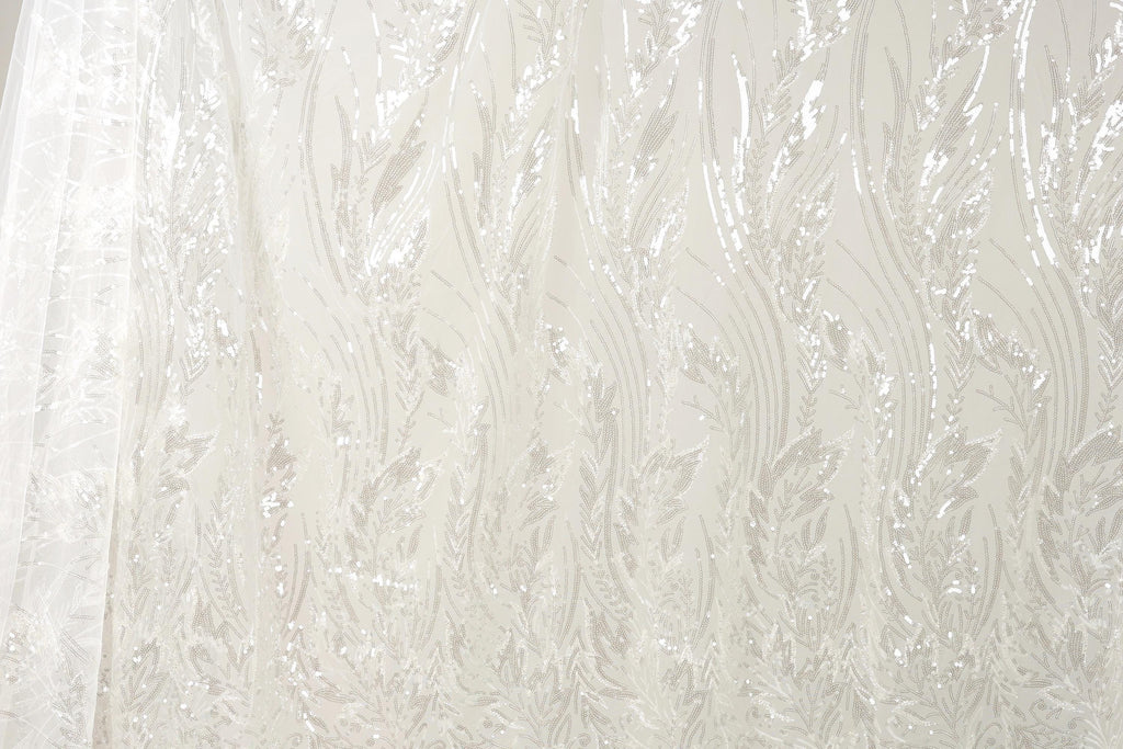 The image is a close-up of a sheer, white fabric with a repeating pattern of leaves or flowers. The fabric appears to be made of sheer material, which is characterized by its delicate and transparent appearance. The pattern on the fabric is intricate and detailed, with the leaves or flowers appearing in varying sizes and orientations, creating a visually appealing and textured effect.
