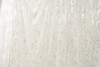 The image is a close-up of a sheer, white fabric with a repeating pattern of leaves or flowers. The fabric appears to be made of sheer material, which is characterized by its delicate and transparent appearance. The pattern on the fabric is intricate and detailed, with the leaves or flowers appearing in varying sizes and orientations, creating a visually appealing and textured effect.