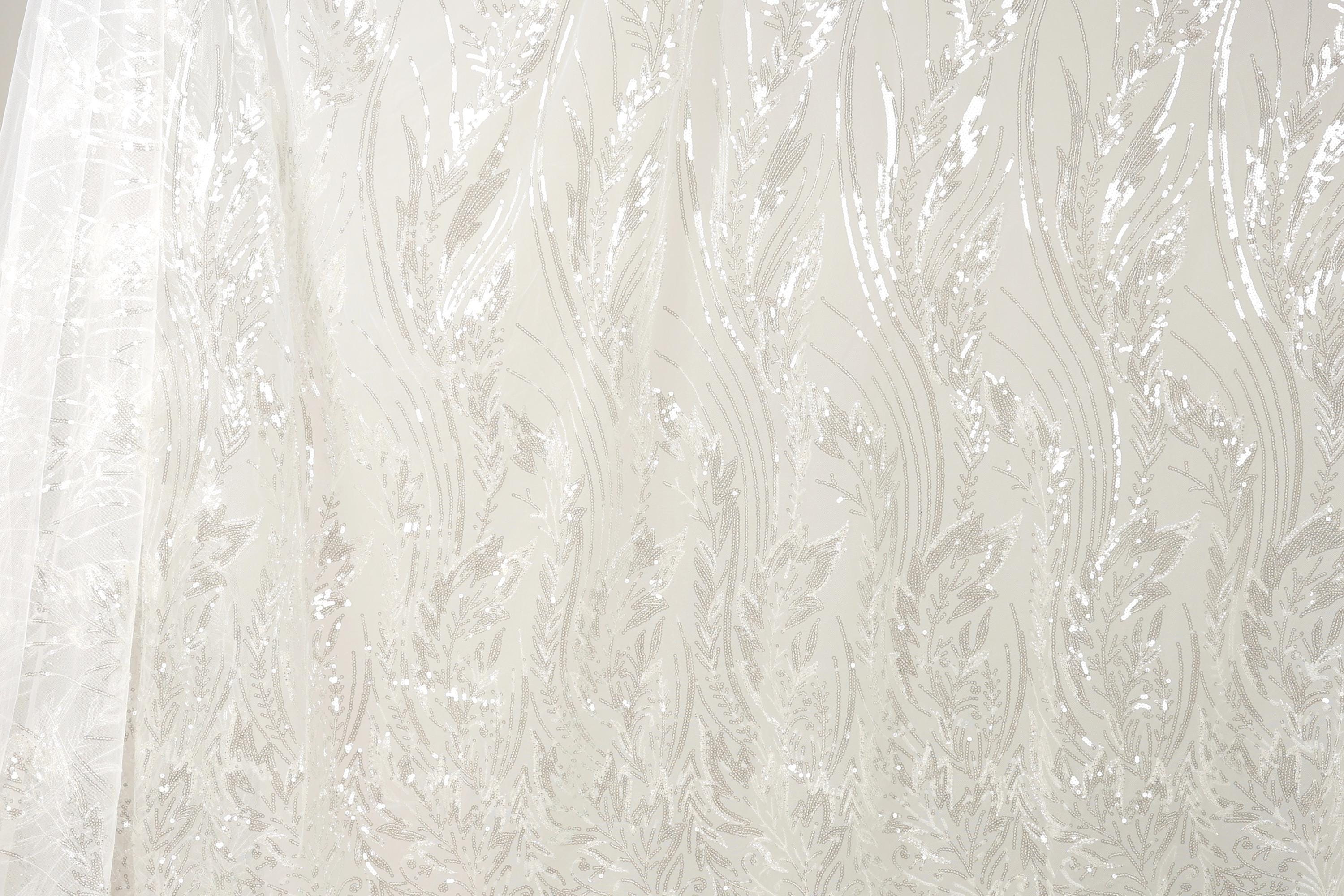 The image is a close-up of a sheer, white fabric with a repeating pattern of leaves or flowers. The fabric appears to be made of sheer material, which is characterized by its delicate and transparent appearance. The pattern on the fabric is intricate and detailed, with the leaves or flowers appearing in varying sizes and orientations, creating a visually appealing and textured effect.