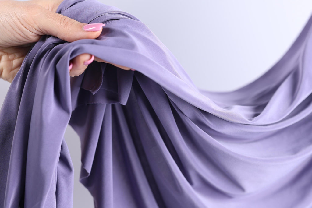 A hand holding a purple fabric, with the fabric being folded and twisted in various ways.