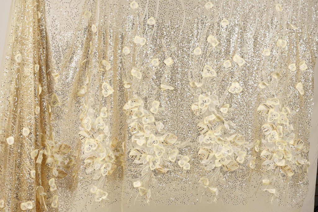 a close-up view of a fabric with a floral pattern, including white and gold flowers. The fabric appears to be made of a shiny, glittery material, giving it a sparkling and elegant appearance.