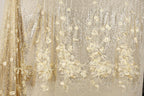 a close-up view of a fabric with a floral pattern, including white and gold flowers. The fabric appears to be made of a shiny, glittery material, giving it a sparkling and elegant appearance.