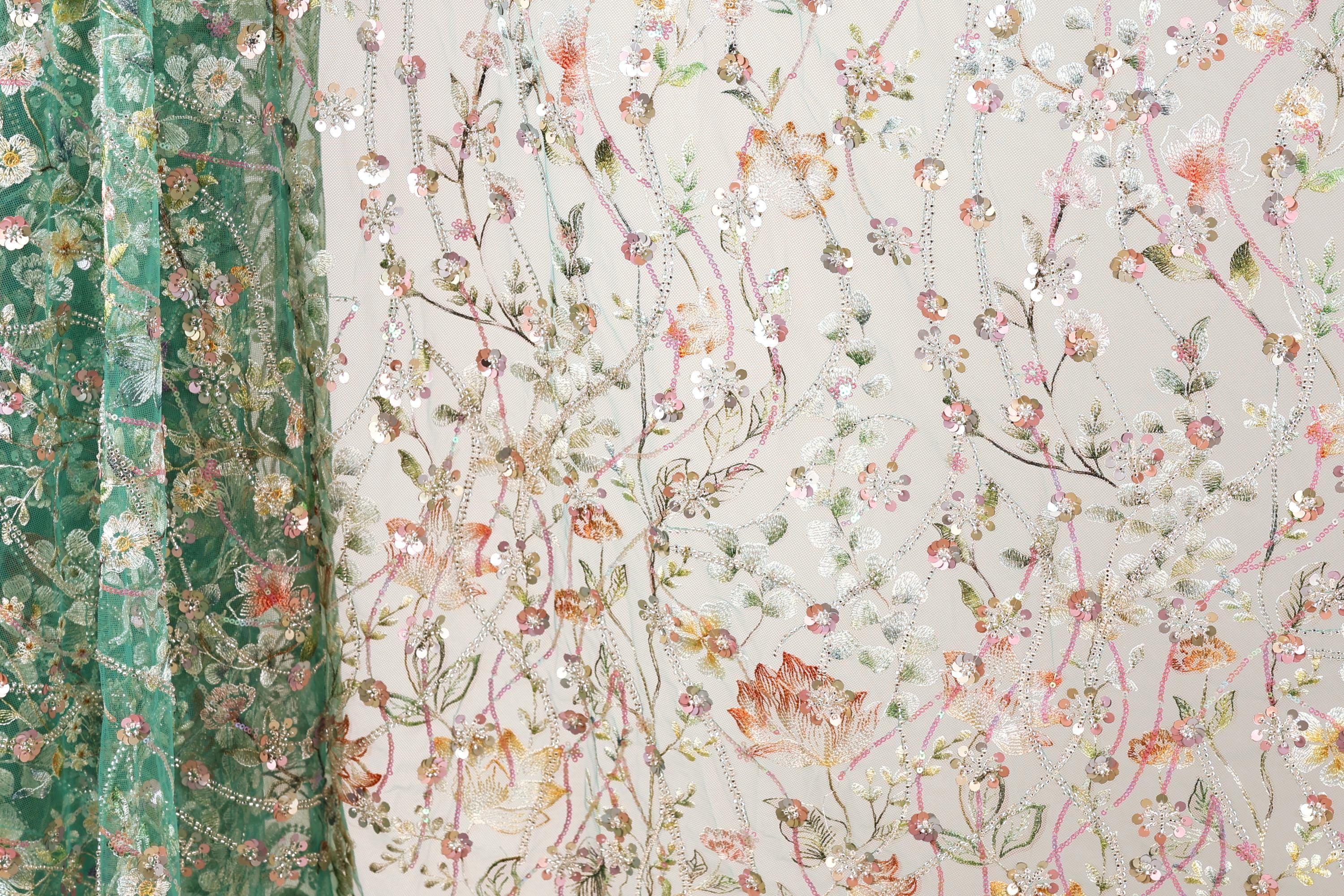 a close-up view of a fabric with a floral pattern, including various shades of green, pink, and white flowers and leaves. The fabric appears to be made of a sheer material, giving it a delicate and airy appearance. The pattern is intricate and detailed, showcasing the craftsmanship involved in creating the fabric.