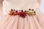 A close-up view of a light pink tulle dress with three decorative flower embellishments on the waistband.