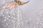 A hand is holding a piece of sheer, white fabric with a leaf pattern, which appears to be a veil or a similar type of garment.