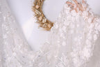 A close-up view of a white lace dress with intricate floral embroidery, featuring a wreath made of dried flowers on the wall behind it.