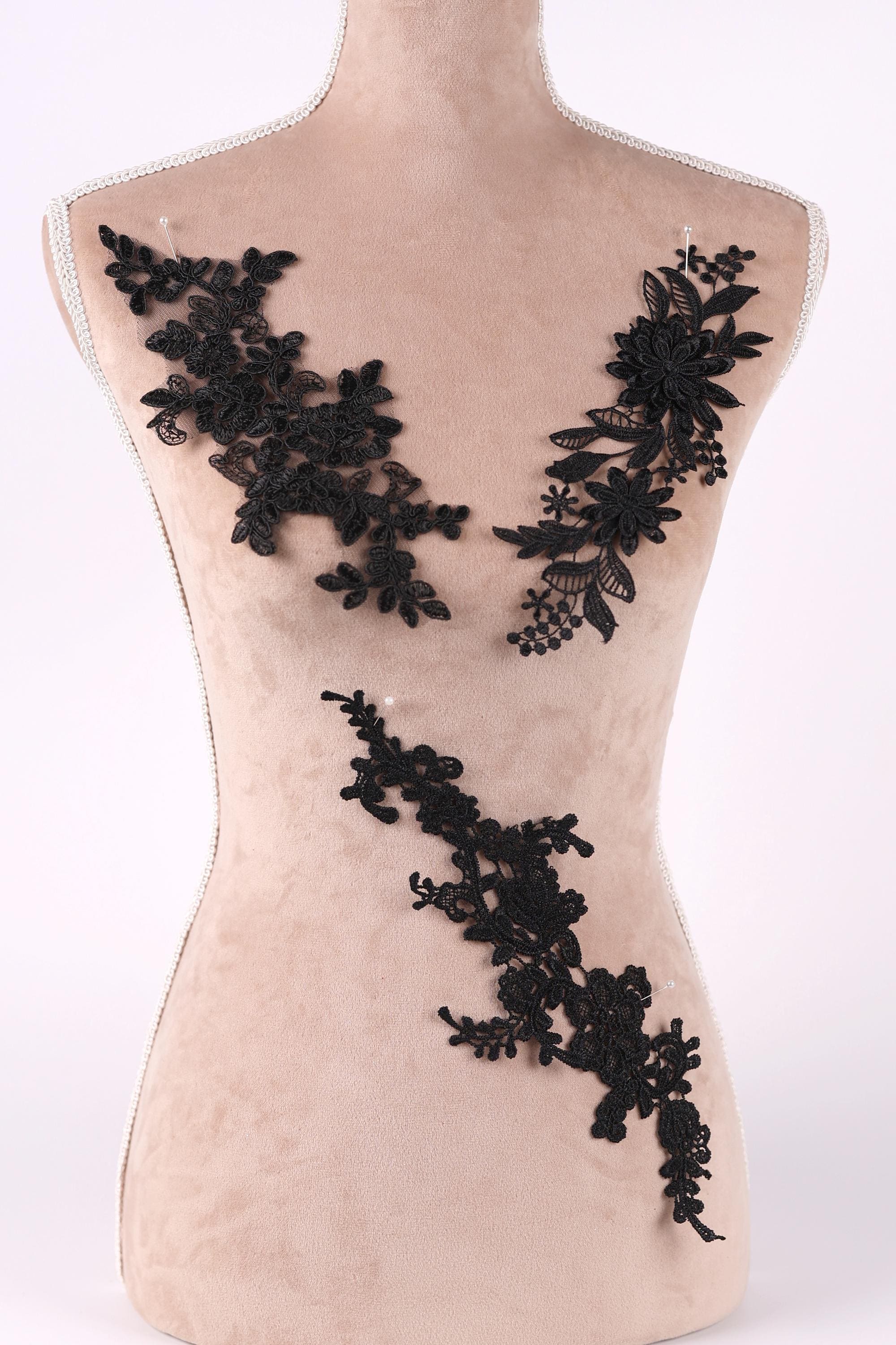 A mannequin torso with black lace appliques on it, including floral and leaf designs.