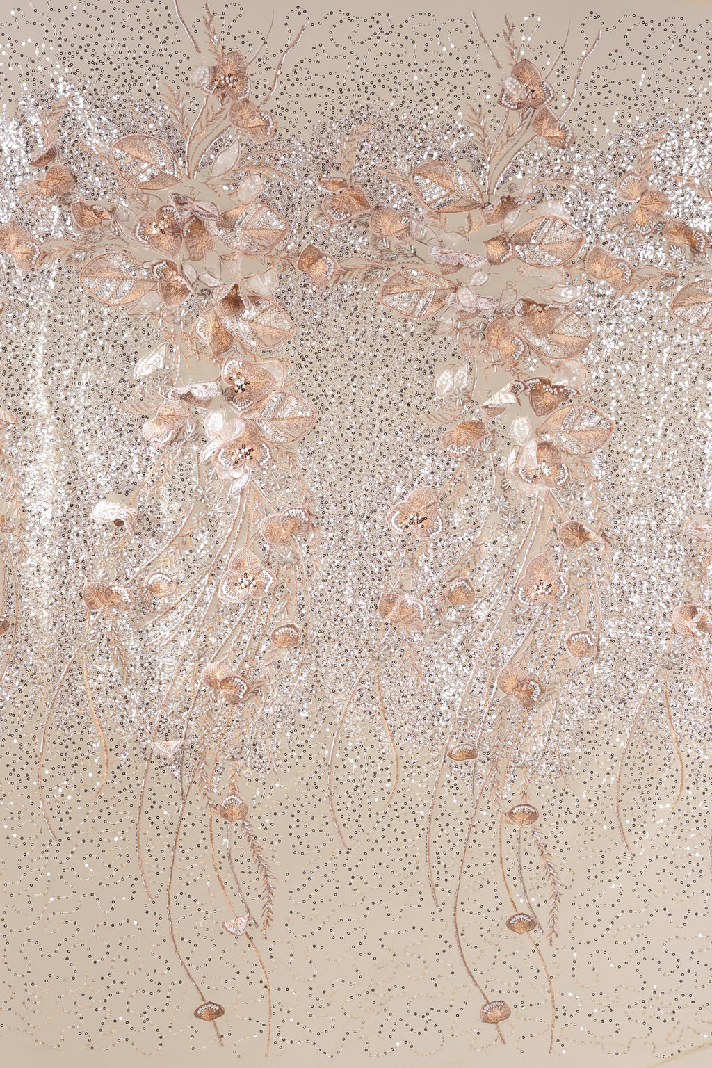 a close-up view of a beige fabric adorned with delicate, shimmering gold and white floral and leaf designs. The intricate patterns and textures create a visually striking and elegant appearance.