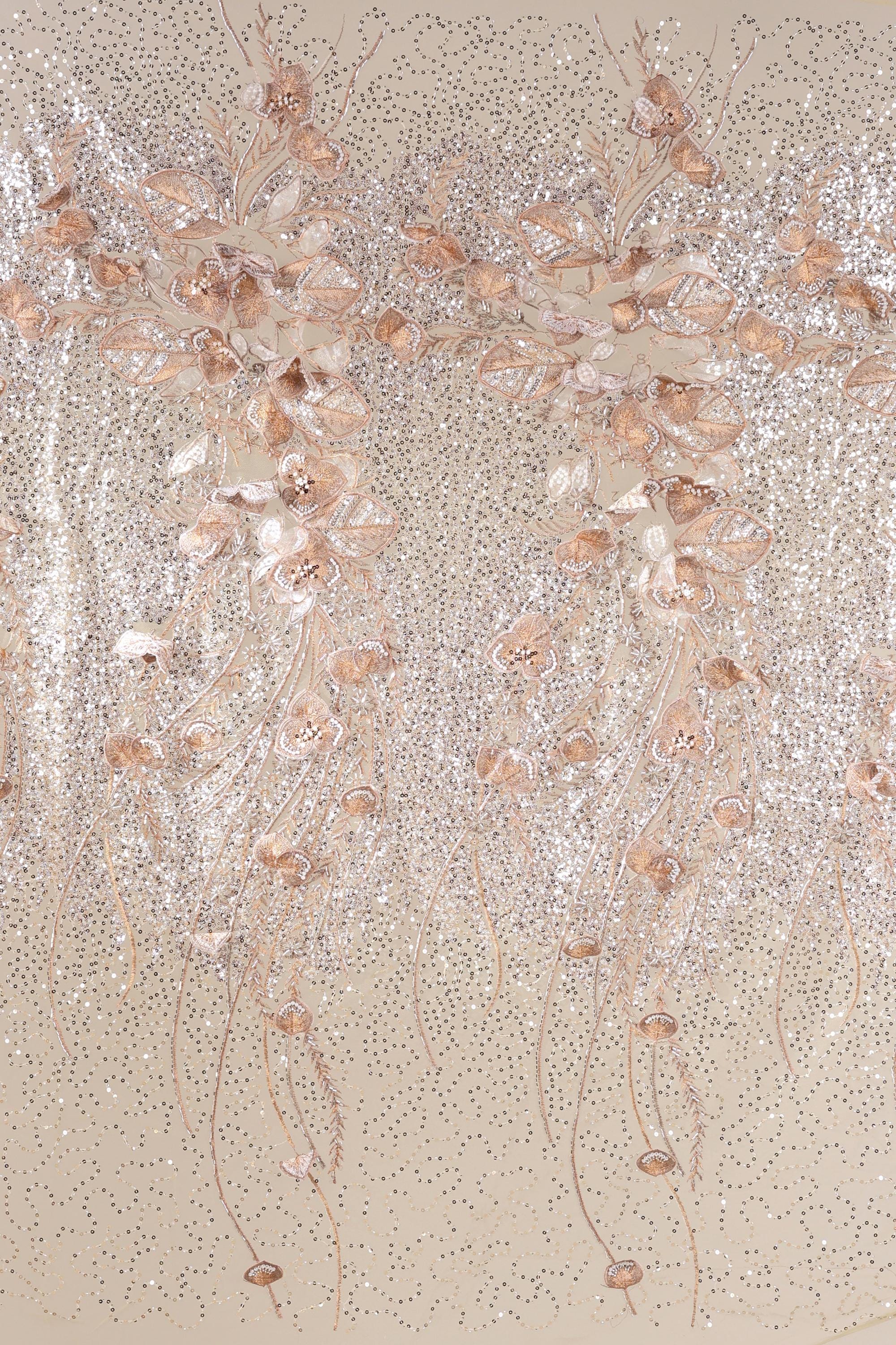 a close-up view of a beige fabric adorned with delicate, shimmering gold and white floral and leaf designs. The intricate patterns and textures create a visually striking and elegant appearance.