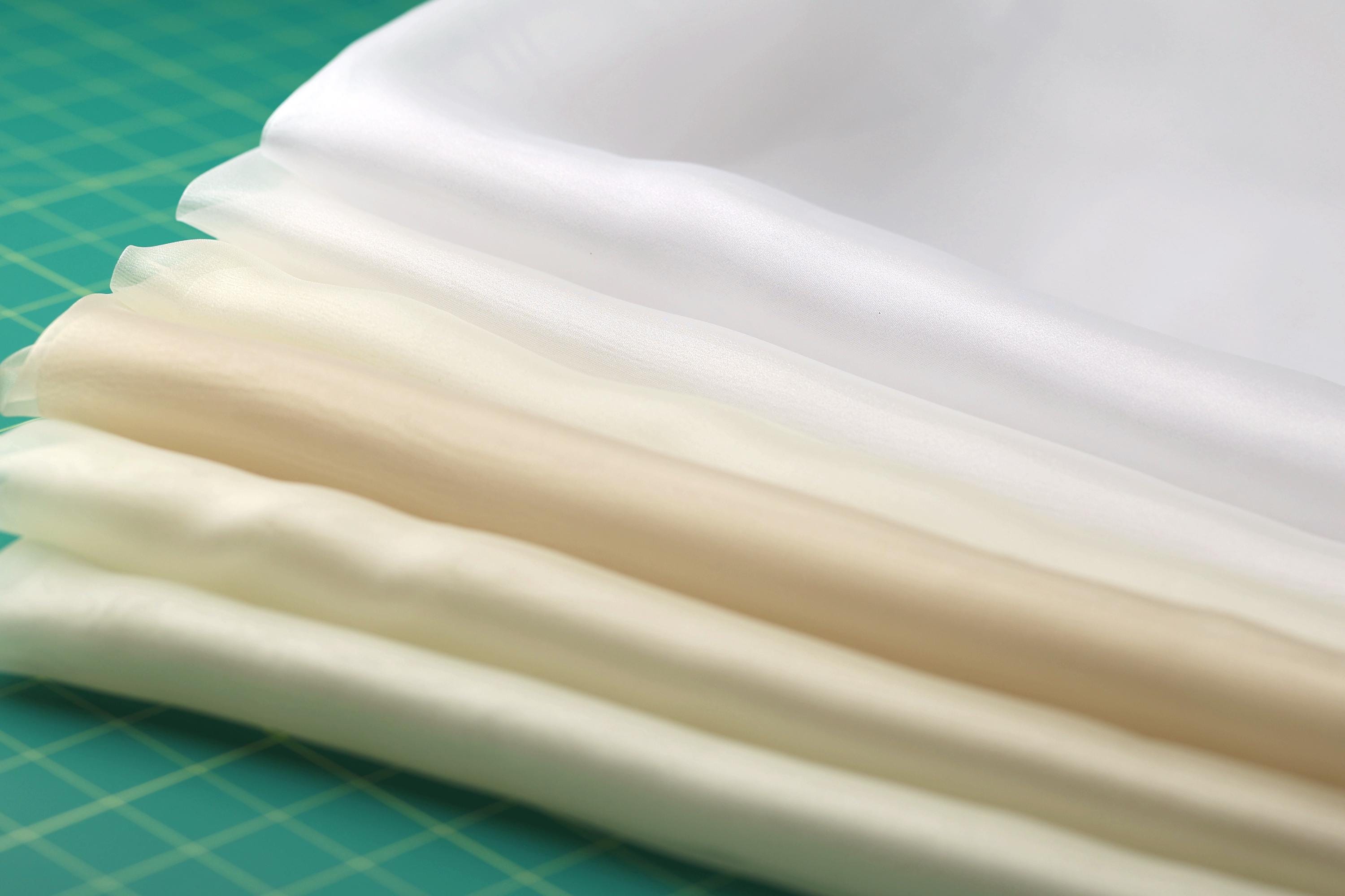 A close-up view of a collection of fabric swatches in various shades of white and beige, arranged on a green surface.