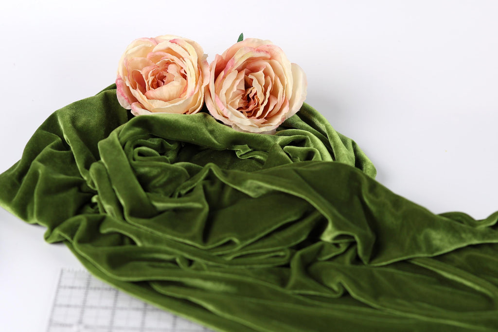 Two pink roses resting on a crumpled green fabric.