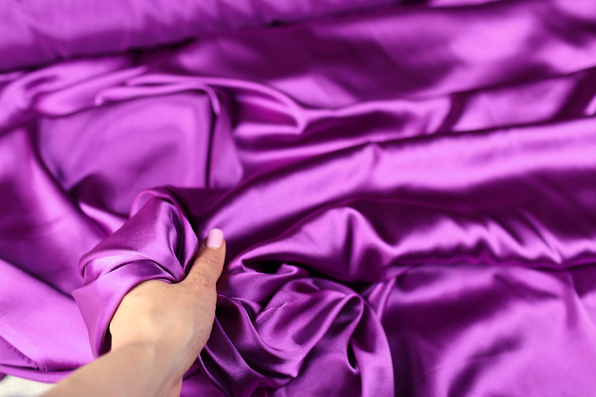 A hand is holding a piece of purple fabric, examining it closely.