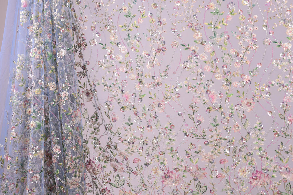 a fabric with a floral pattern, including various types of flowers and leaves. The fabric appears to be a sheer material, with a delicate and intricate design.