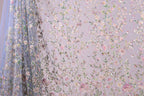 a fabric with a floral pattern, including various types of flowers and leaves. The fabric appears to be a sheer material, with a delicate and intricate design.