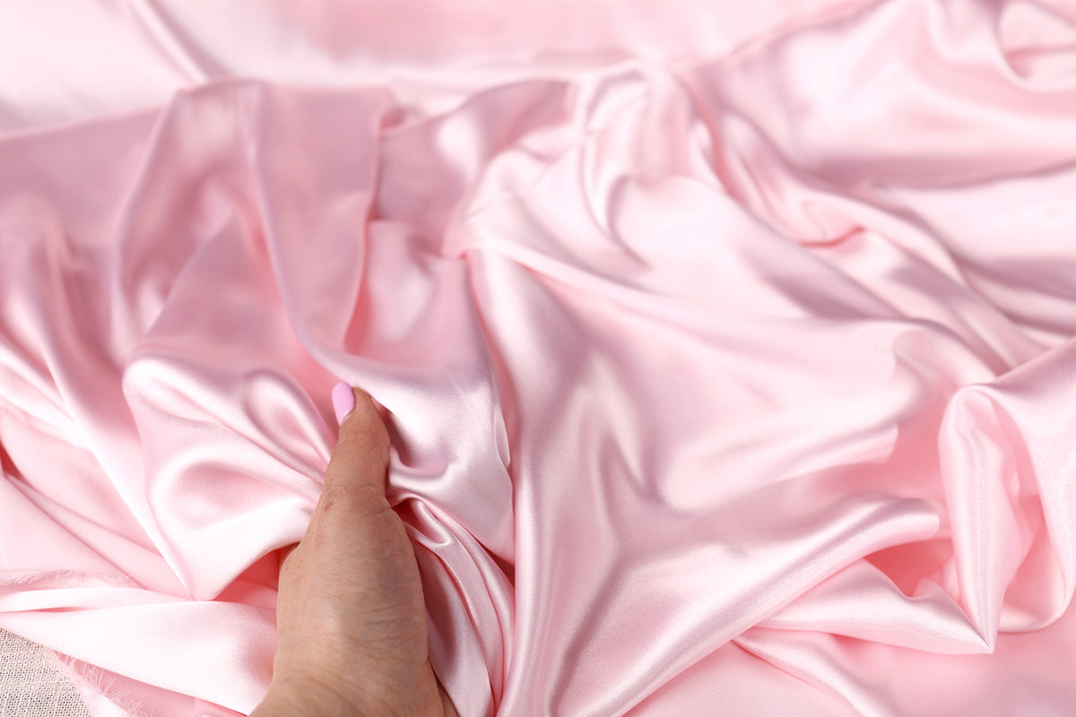 A hand is holding a piece of pink satin fabric, gently touching it.