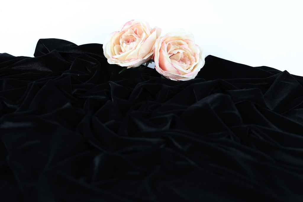 Two pink roses resting on a crumpled black fabric.