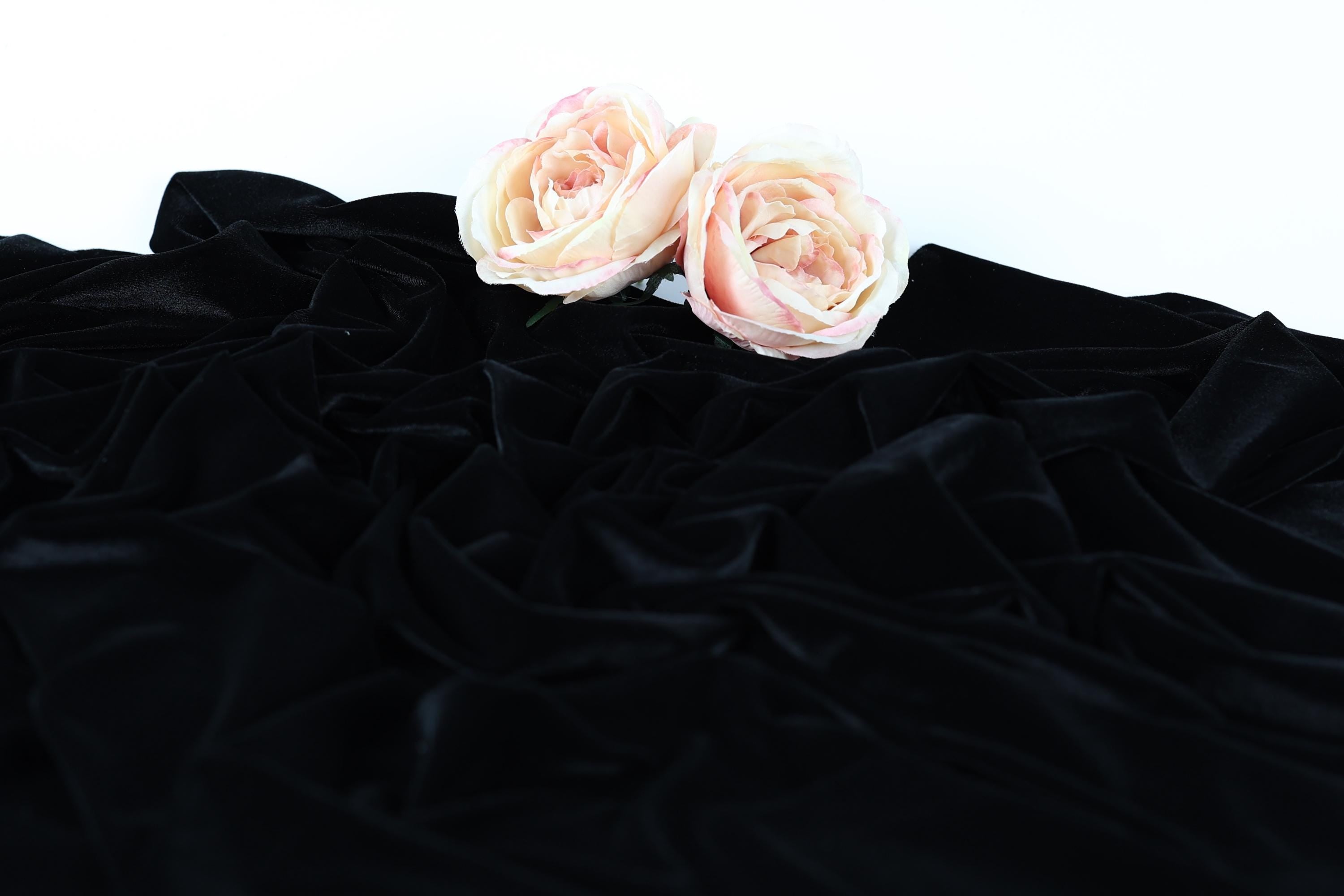Two pink roses resting on a crumpled black fabric.