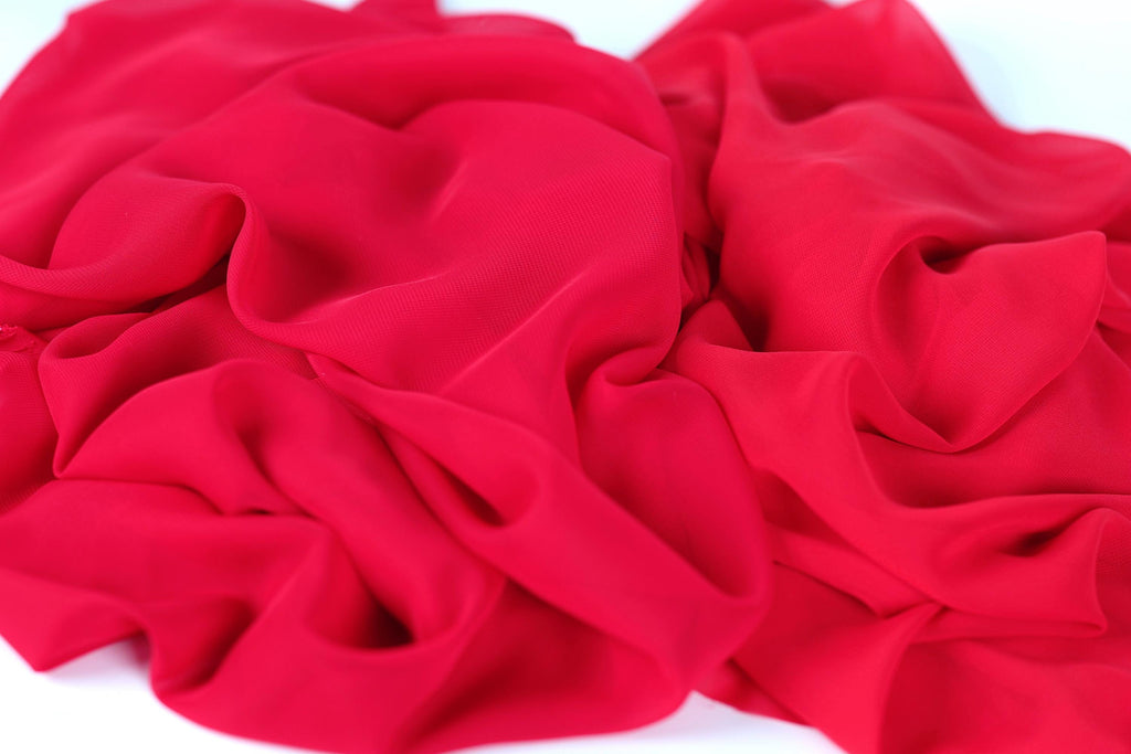 The image is a close-up of a red fabric, possibly silk or chiffon, with a crumpled and wrinkled texture.
