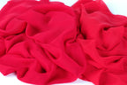 The image is a close-up of a red fabric, possibly silk or chiffon, with a crumpled and wrinkled texture.