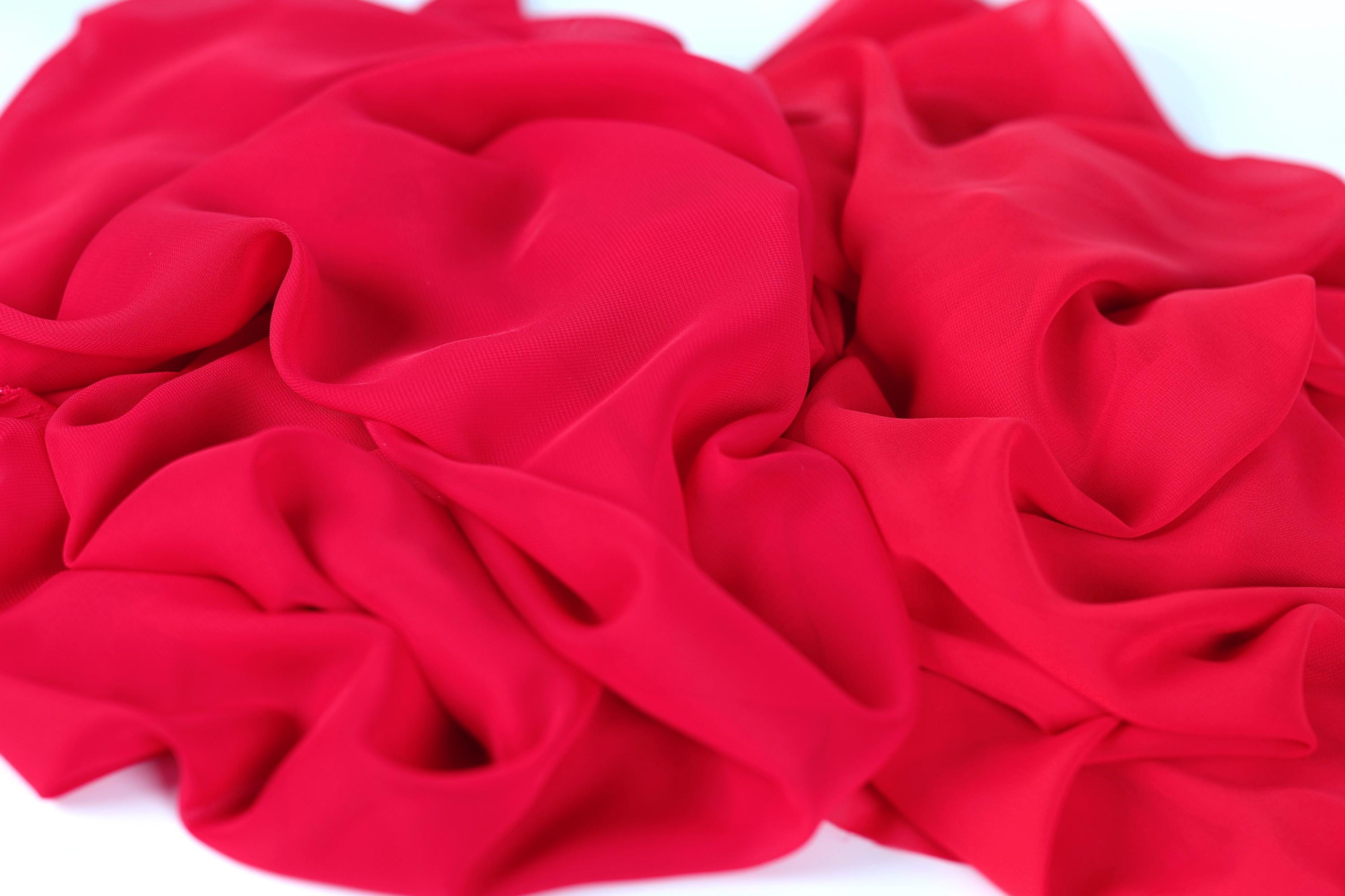 The image is a close-up of a red fabric, possibly silk or chiffon, with a crumpled and wrinkled texture.