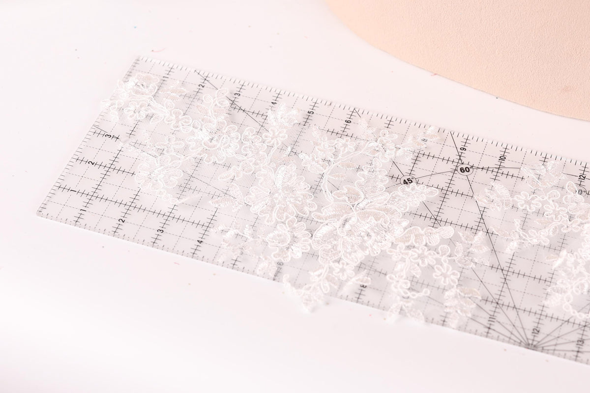 a close-up view of a clear ruler with a lace pattern on it, placed on a white surface.