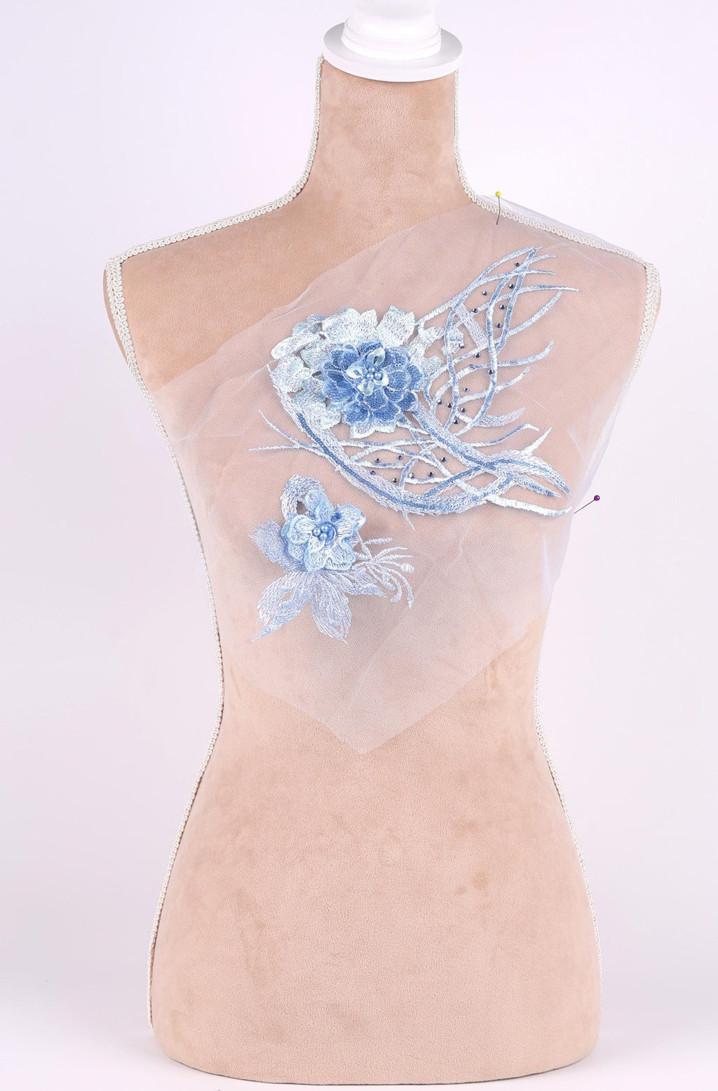 A mannequin with a beige body and a white head, wearing a white fabric with blue floral embroidery.