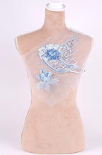 A mannequin with a beige body and a white head, wearing a white fabric with blue floral embroidery.