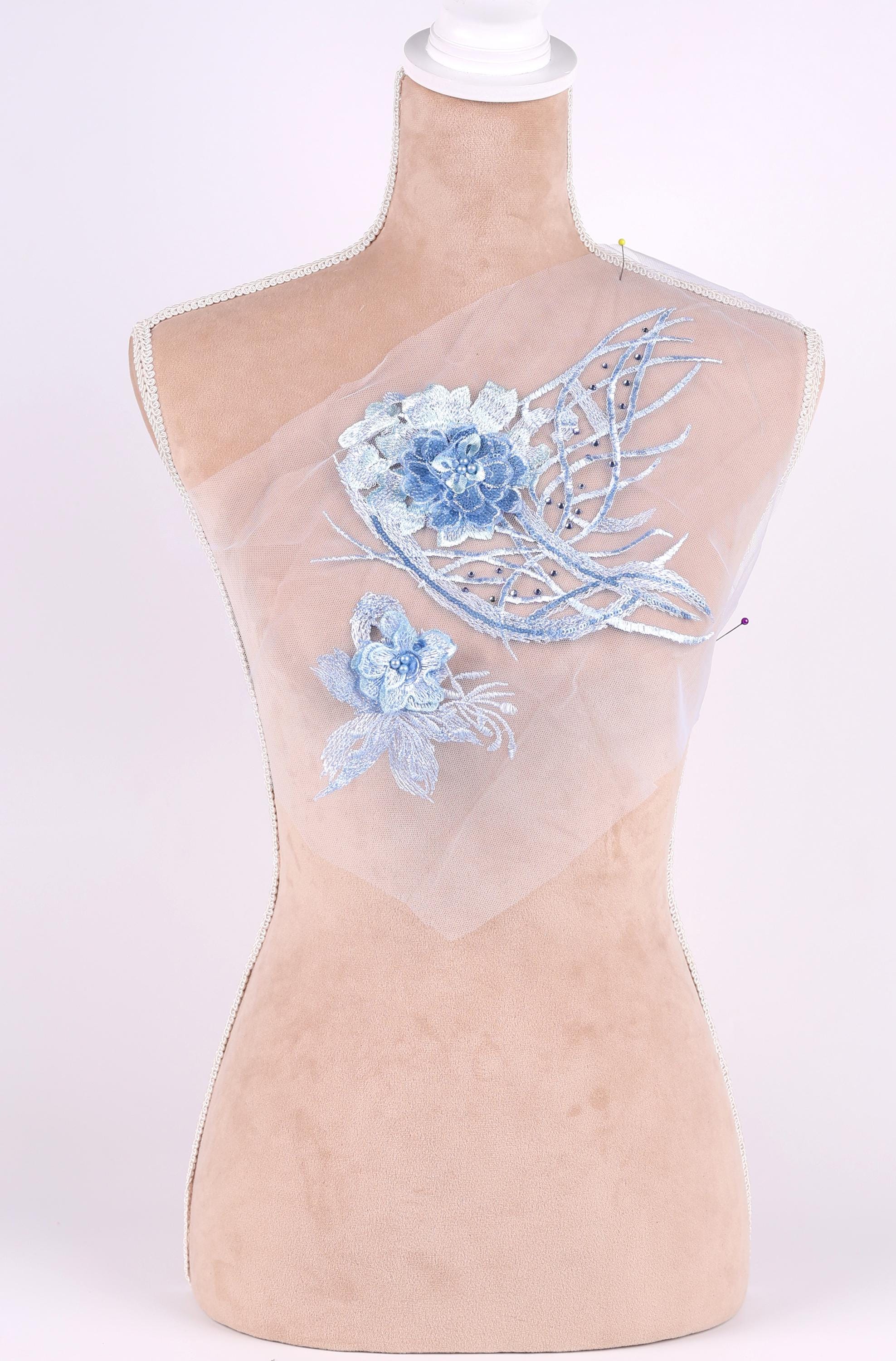 A mannequin with a beige body and a white head, wearing a white fabric with blue floral embroidery.