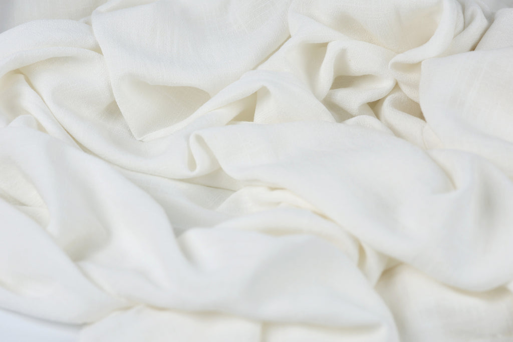 The image is a close-up of a white fabric, possibly a piece of clothing or a textile, with a slightly crumpled and wrinkled appearance.