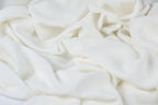 The image is a close-up of a white fabric, possibly a piece of clothing or a textile, with a slightly crumpled and wrinkled appearance.